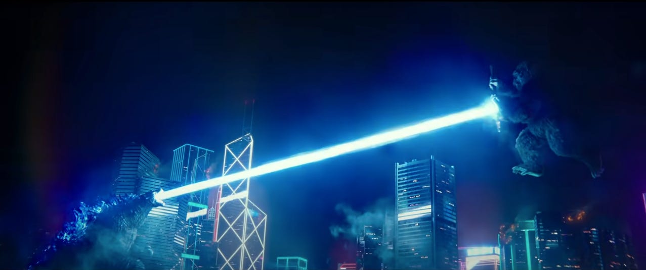 From the film 'Godzilla vs. Kong': Towering over Hong Kong buildings at night, Godzilla fires atomic breath at a charging King King, who is blocking with a special axe.