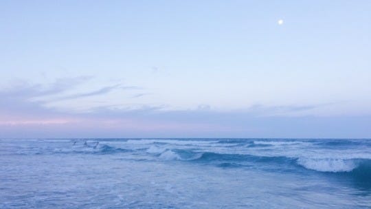 image of the sea at sunset, with varying shades of blue for the sky and sea. near the horizon there is a streak of pink.