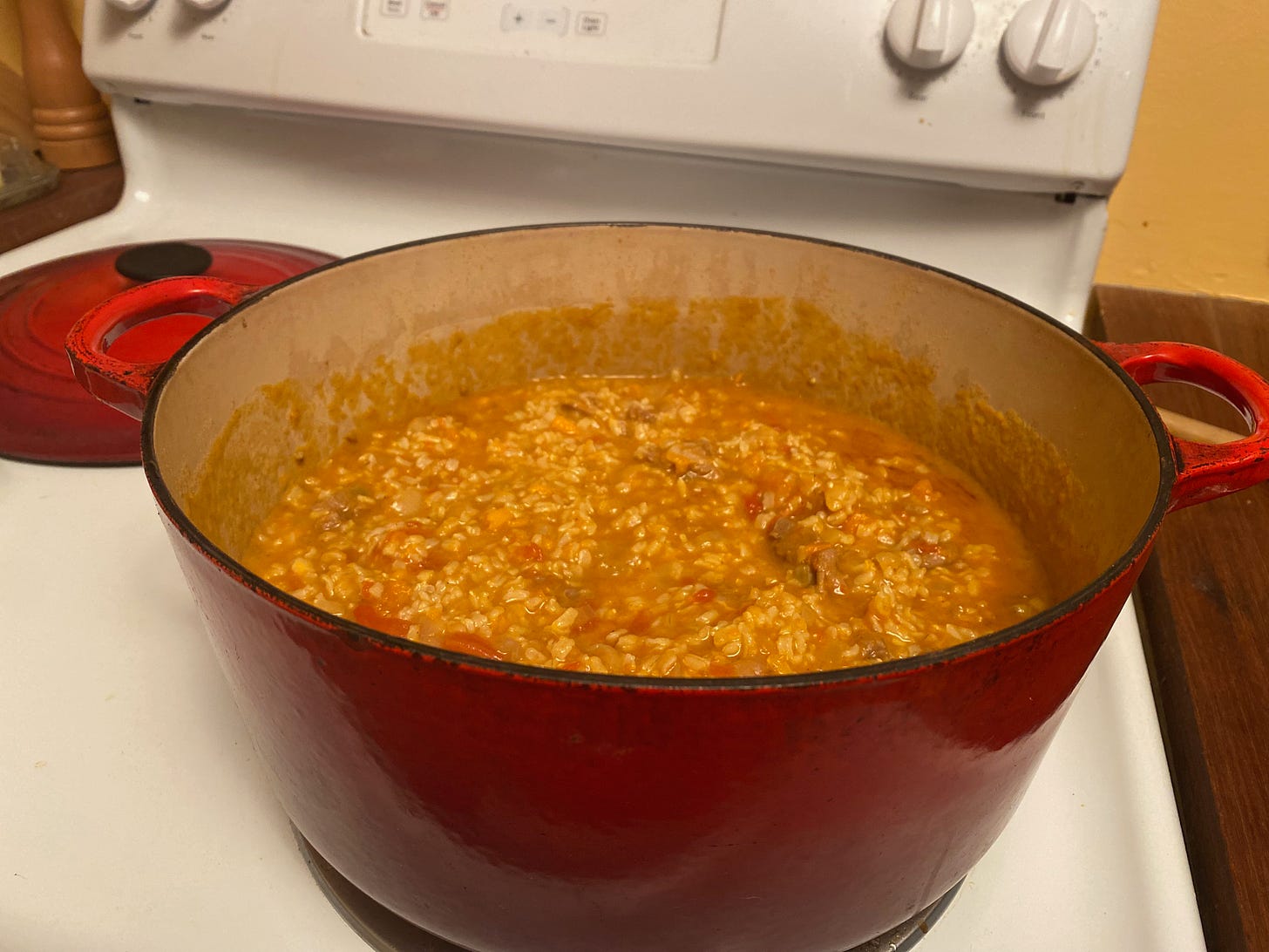 A large red Dutch oven full of lamb curry mixed with rice sits on a stove.