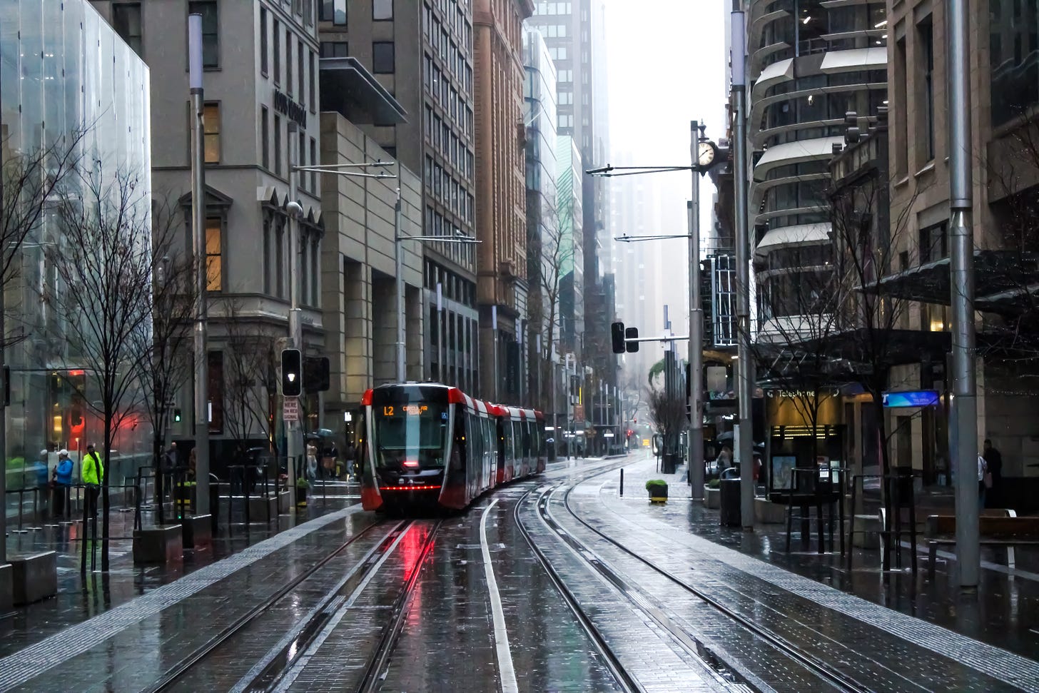 Sydney in the rain, photo taken in 2020. The road is wet and empty. A light rail is running.