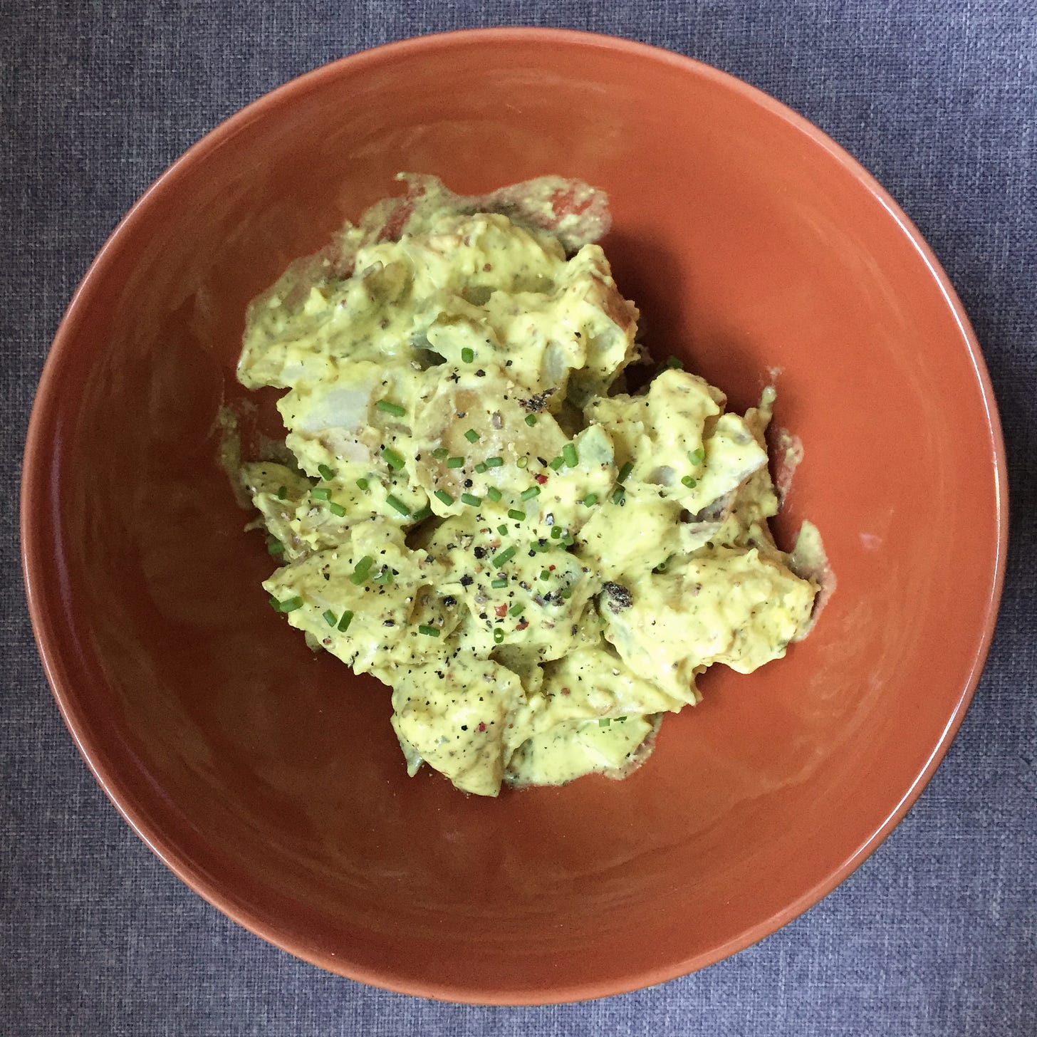 an orange bowl of yellowy potato salad, topped with minced chives and ground pepper.