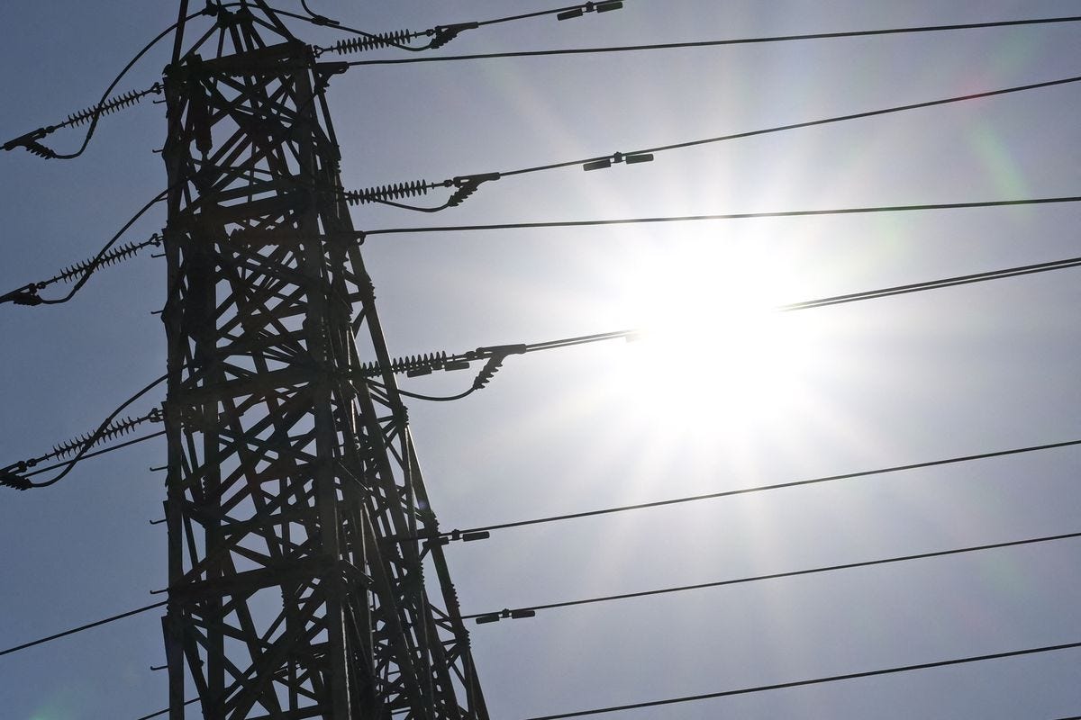 The sun shines behind electrical power lines.