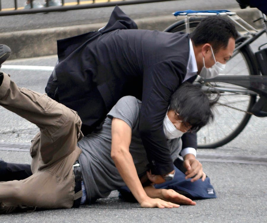 Tetsuya Yamagami, bottom, is detained near the site of gunshots in Nara Prefecture, western Japan, Friday, July 8, 2022.