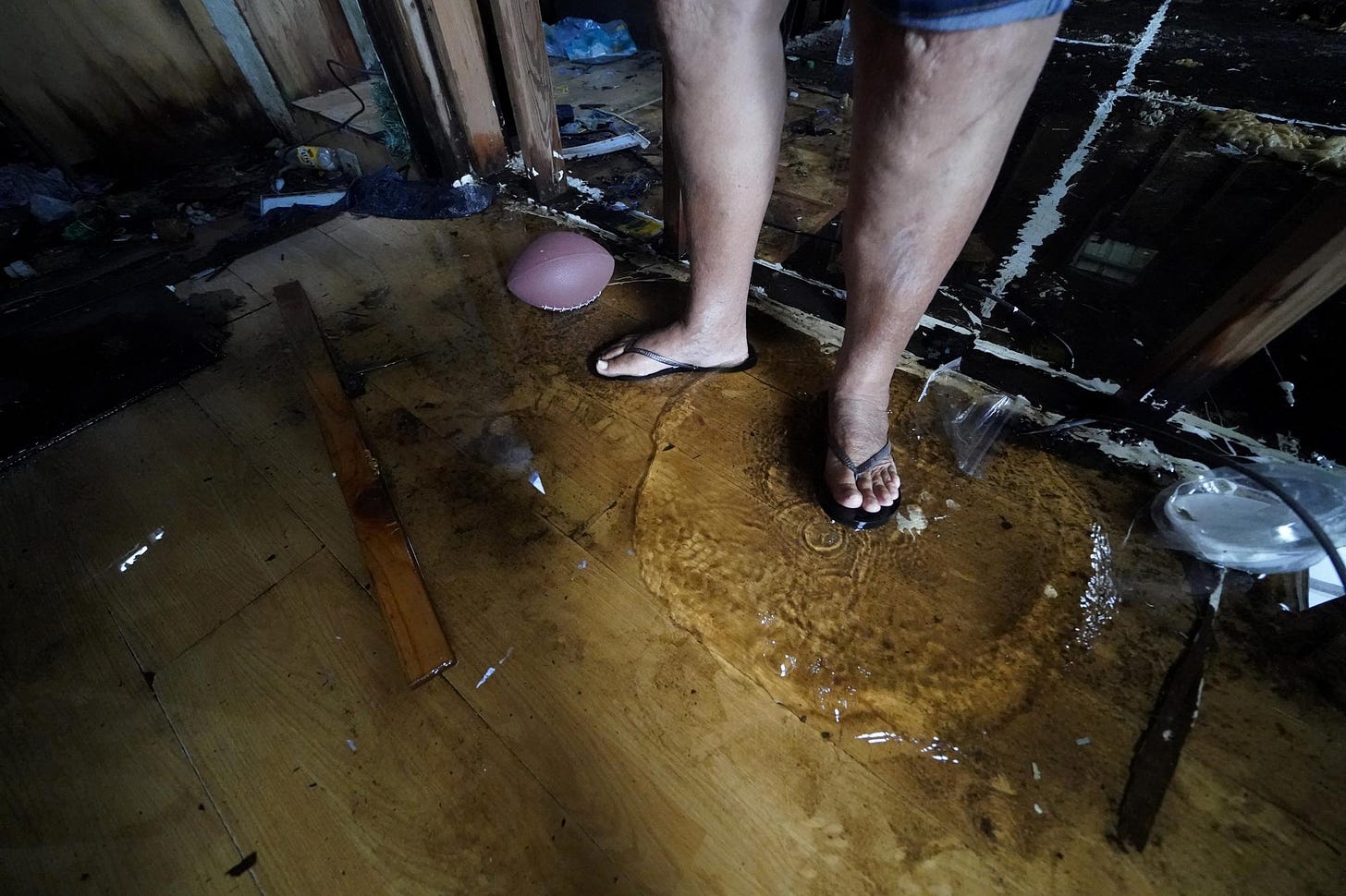 Standing water from roof holes splashes on the plywood sub-floor as Irene Verdin talks inside her home that was heavily damaged by Hurricane Ida nine months before, along Bayou Pointe-au-Chien, La., Tuesday, May 24, 2022. (AP Photo/Gerald Herbert)