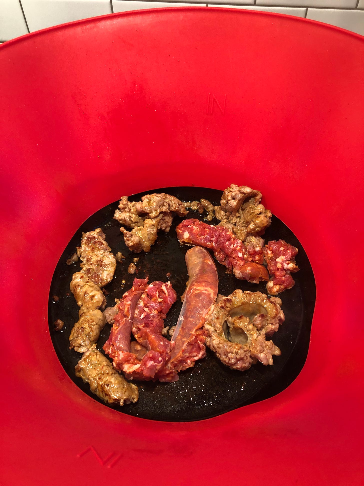 Sausages browning in a skillet, surrounded by a red silicone ring.