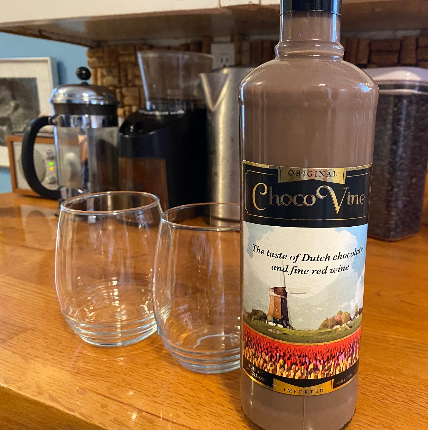 Bottle of ChocoVine (liquid the color of chocolate milk) and two empty stemless wine glasses. 