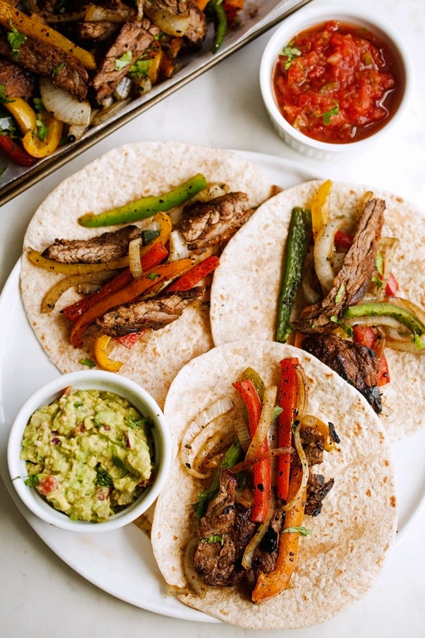 beef fajitas with peppers and onions on tortillas with bowls of guacamole and salsa