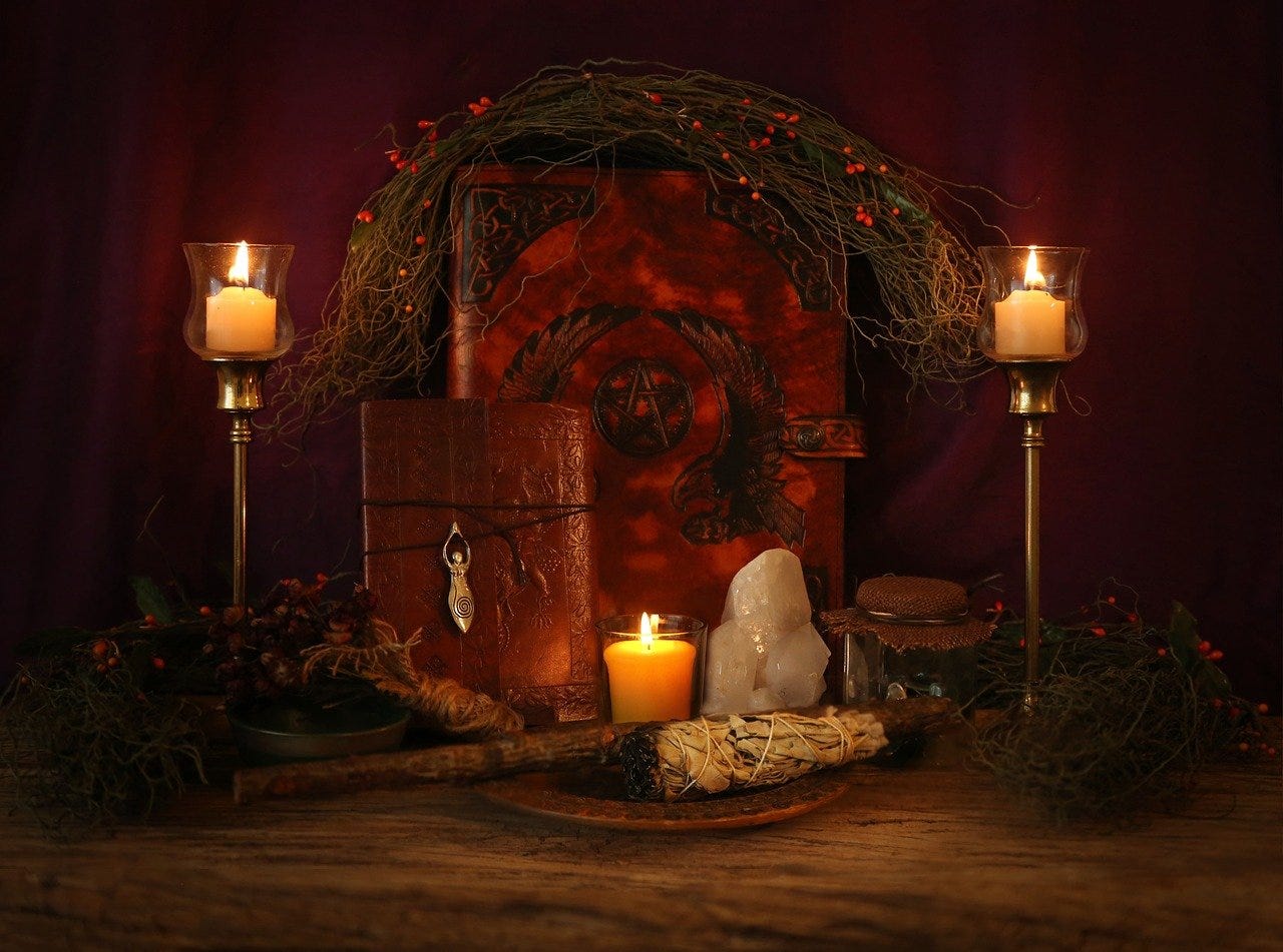 A pagan-ish Christmas scene is here, which the author will give her best Christian attempt to accurately describe. A arkened room sees a leather journal with a pentagram on it, surrounded by a twig and berries wreath. Maybe it's a spell book? In front of that is a small leather journal wrapped in twine, with a little crystal thingy, and a white candle in a glass jar. Next to it is a white crstal, and then a little jar wrapped in twine material with maybe more crystals in it? In front of THAT is burning sage stuff, see, I know this one. Finally there's more twigs and berries and maybe a little bit of holly surrounding the whole scene, framed by two more candles, except these two are in long silver candlesticks too.