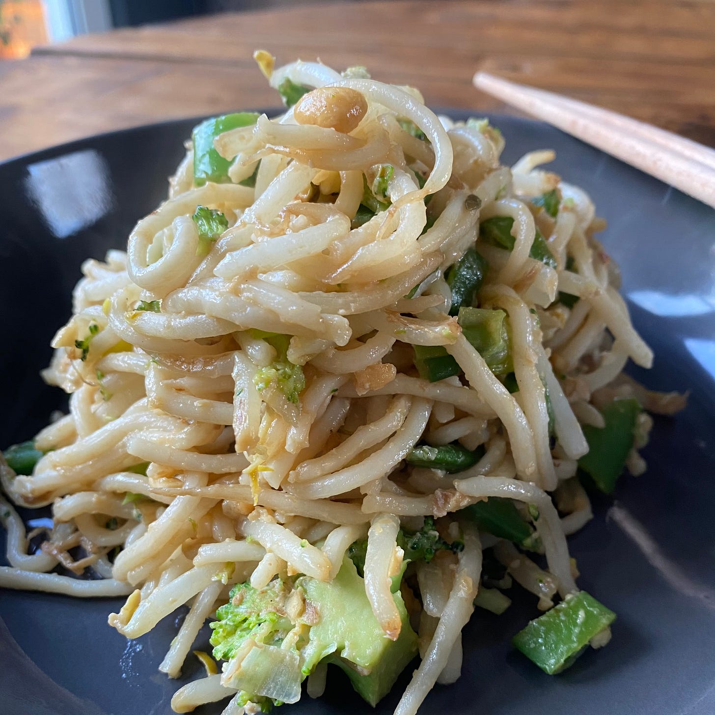 Bowl of noodles with broccoli, sugar snaps, bean sprouts and peanuts