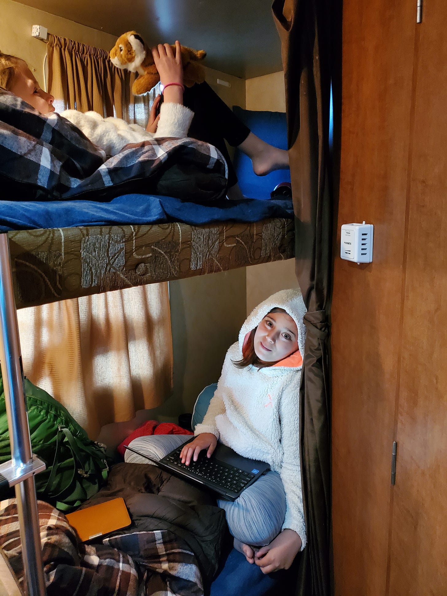 Interior shot of the travel trailer. One girl in the upper bunk and one girl in the lower bunk bed.