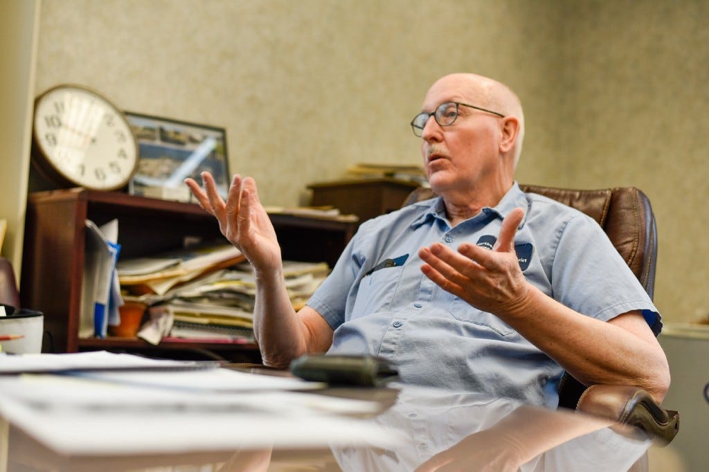 Bob Bonnett talks with his hands as he reclines in his office recounting his earliest days in his Sewer District career. Blurred behind him is book shelf filled with file folders, reports, and papers.