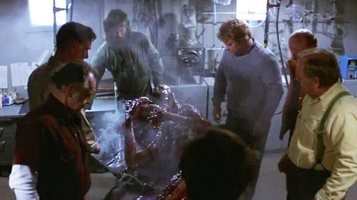 7 men in a infirmary gathered around the steaming, raw and vaguely human remains of the shapeshifting Thing.