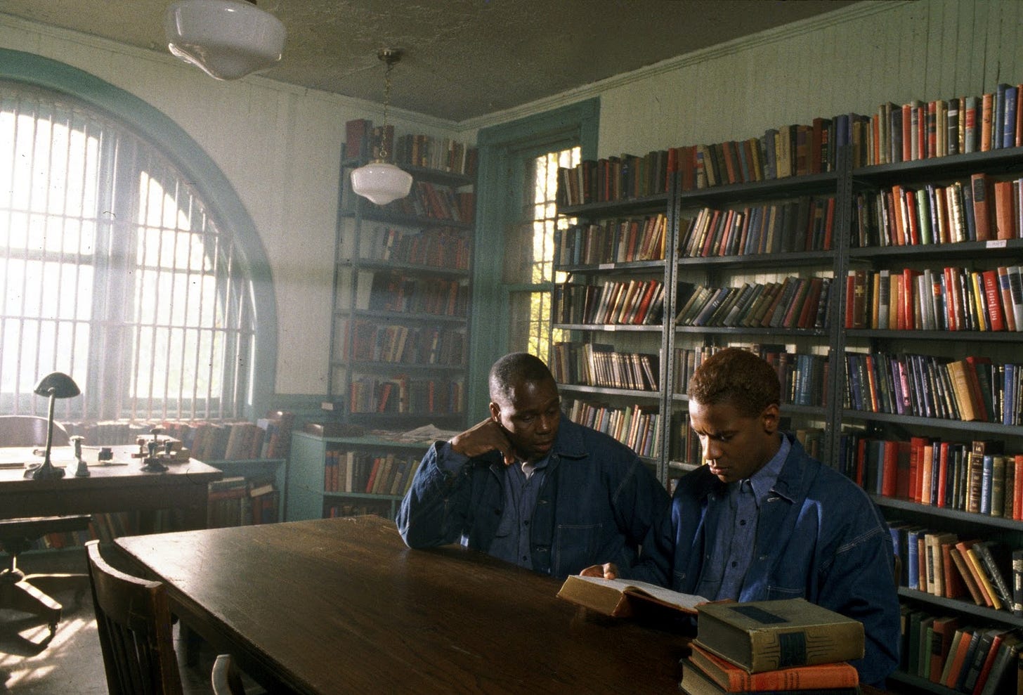 This image shows the character Baines (played by Albert Hall) and Malcolm "Red" Little (played by Denzel Washington) sitting and chatting inside a prison library. Several bookshelves sit behind them, while Malcolm examines a dictionary in one of the best (and most famous) sequences from Spike Lee's 1992 film Malcolm X. This image shows the character Baines (played by Albert Hall) and Malcolm "Red" Little (played by Denzel Washington) sitting and chatting inside a prison library. Several bookshelves sit behind them, while Malcolm examines a dictionary in one of the best (and most famous) sequences from Spike Lee's 1992 film Malcolm X.