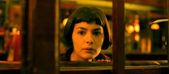 A close-up of a woman's face as she peers out a window. She has short brown hair, brown eyes, and a neutral expression.
