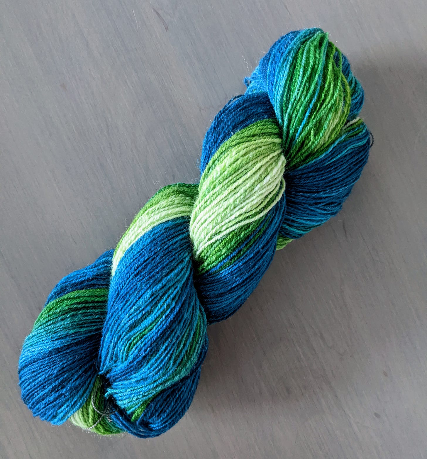 A skein of variegated yarn ranging from pale green to dark blue on a gray background