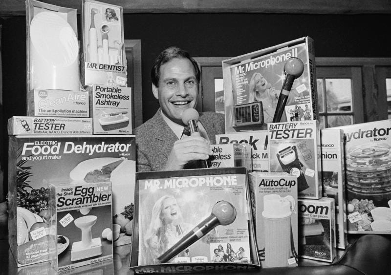 FILE - In this Wednesday, Dec. 8, 1982 file photo, Ron Popeil, the man behind those late-night, rapid-fire television commercials that sell everything from the Mr. Microphone to the Pocket Fisherman to the classic Veg-a-Matic, sits surrounded by his wares in his office in Beverly Hills, Calif.  Ron Popeil, the quintessential TV pitchman and inventor known to generations of viewers for hawking products including the Veg-O-Matic, the Chop-O-Matic, Mr. Microphone and the Showtime Rotisserie and BBQ, died Wednesday, July 28, 2021 his family said. (AP Photo/Reed Saxon, File)