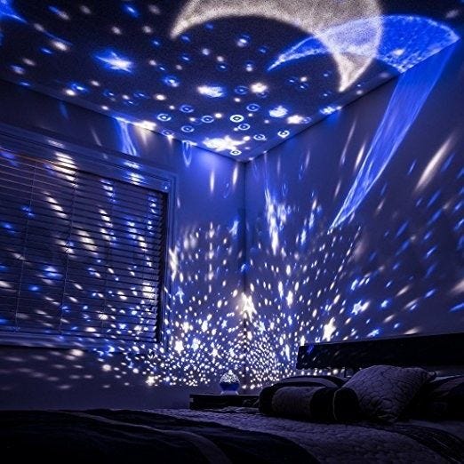 A dark bedroom lit in shades of blue with white stars and moons projected on the walls and ceiling. 