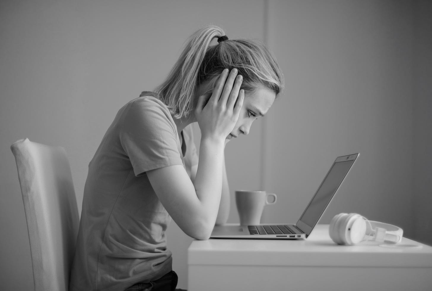 A slender young woman with her hands to her face, looks worried as she stares into her laptop computer screen