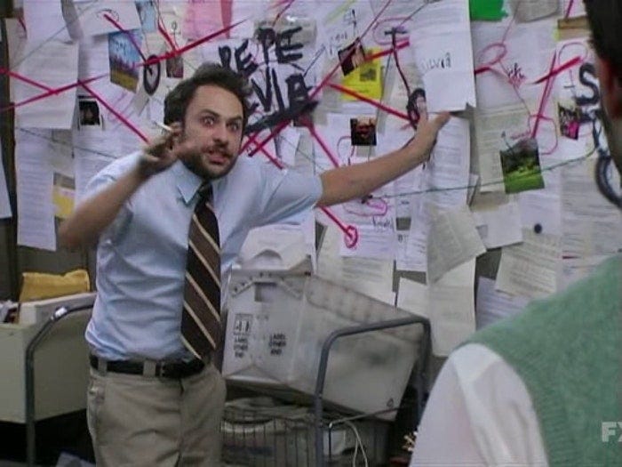 The image from "It's Always Sunny" of Charlie Kelly, played by Charlie Day, standing in front of a cork board with papers pinned up in an array, linked together with red string, spray painted in black "Pepe Silvia" over the papers. He looks exhausted and crazed.