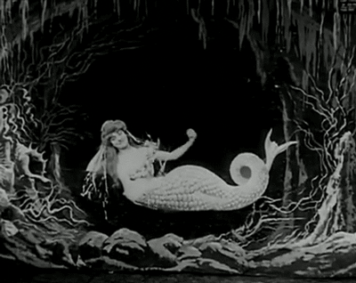 Black and white, grainy GIF of a woman in a mermaid costume blowing a kiss.