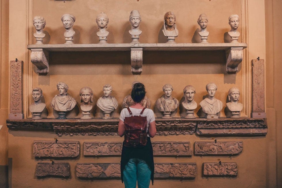person standiing in front of a wall full of bust sculptures