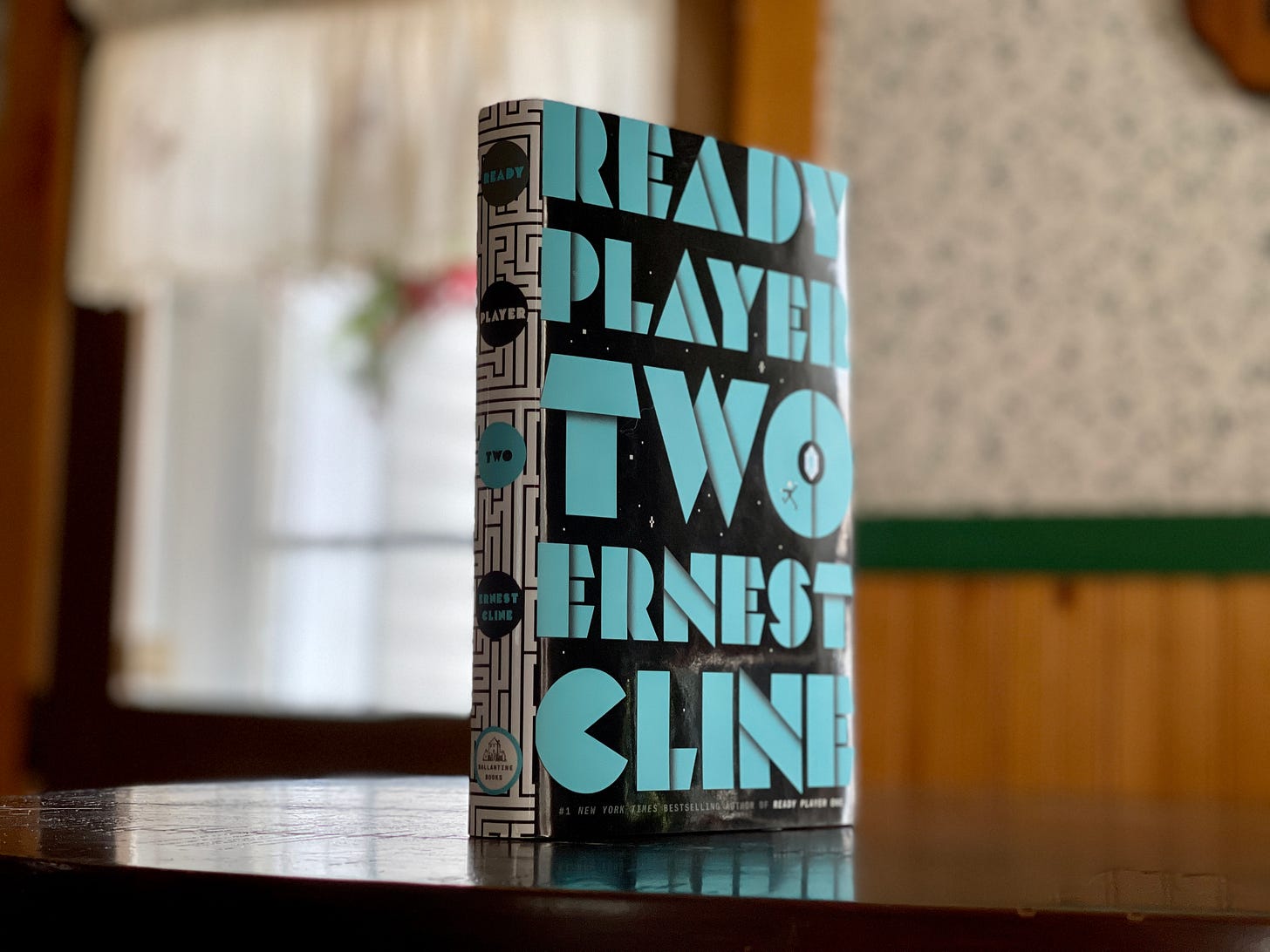 A single copy of Ready Player Two, title and author listed in light blue on a black background, stands on a kitchen table. 