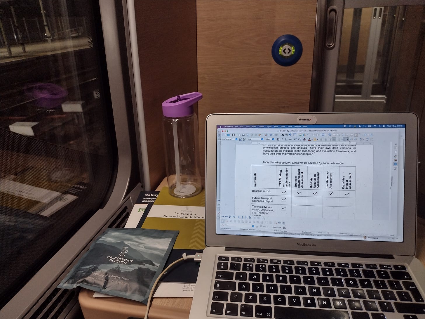 On board the sleeper train. There is a laptop and water flask on a small table, with a window to the left