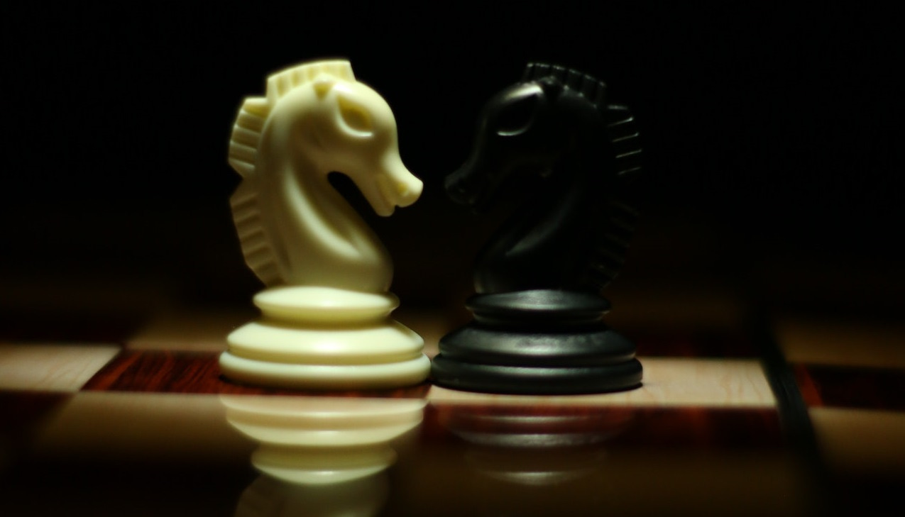 Two opposing knights on a dimly lit chess board.