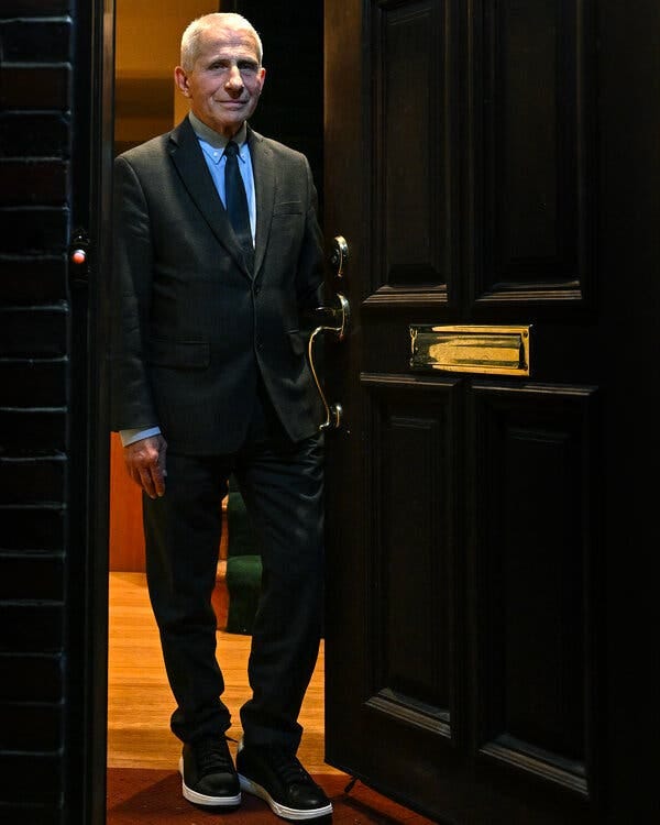 Dr. Anthony S. Fauci standing in the doorway to his home wearing a suit and sneakers.