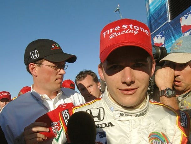 Rob Cleveland in the background as the late Dan Wheldon talks to reporters. Photo by Tom Savage