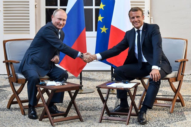 Macron and Putin shaking hands with the French, EU and Russian flags behind them.