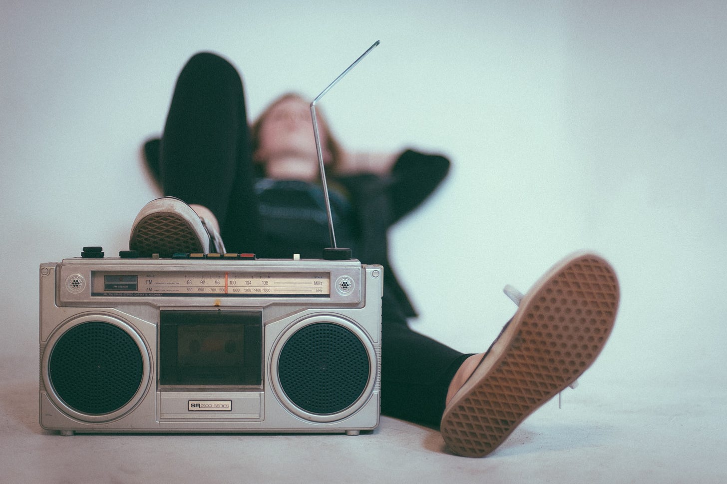 Man laying down with his sneaker up on a boom box. Background is plain white.