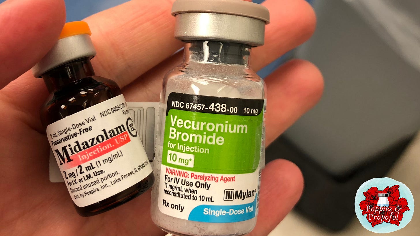 A close up of a hand holding two vials - an amber midazolam vial with orange cap, and a clear vecuronium vial with beige top.