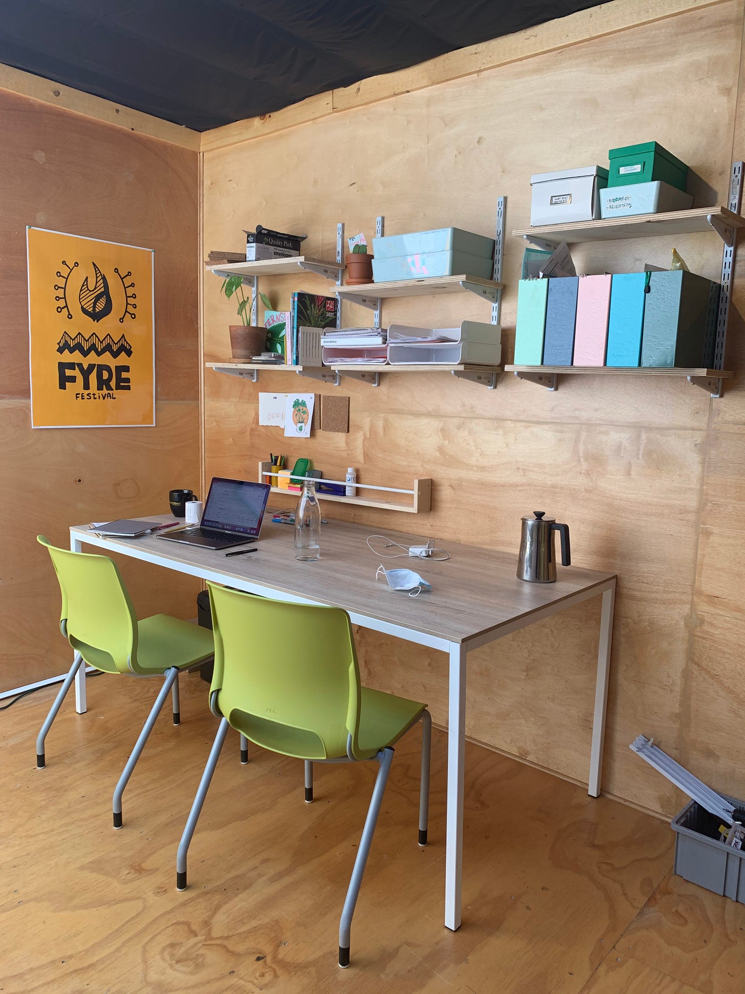 tidy office desk with yellow FYRE Festival poster on the wall