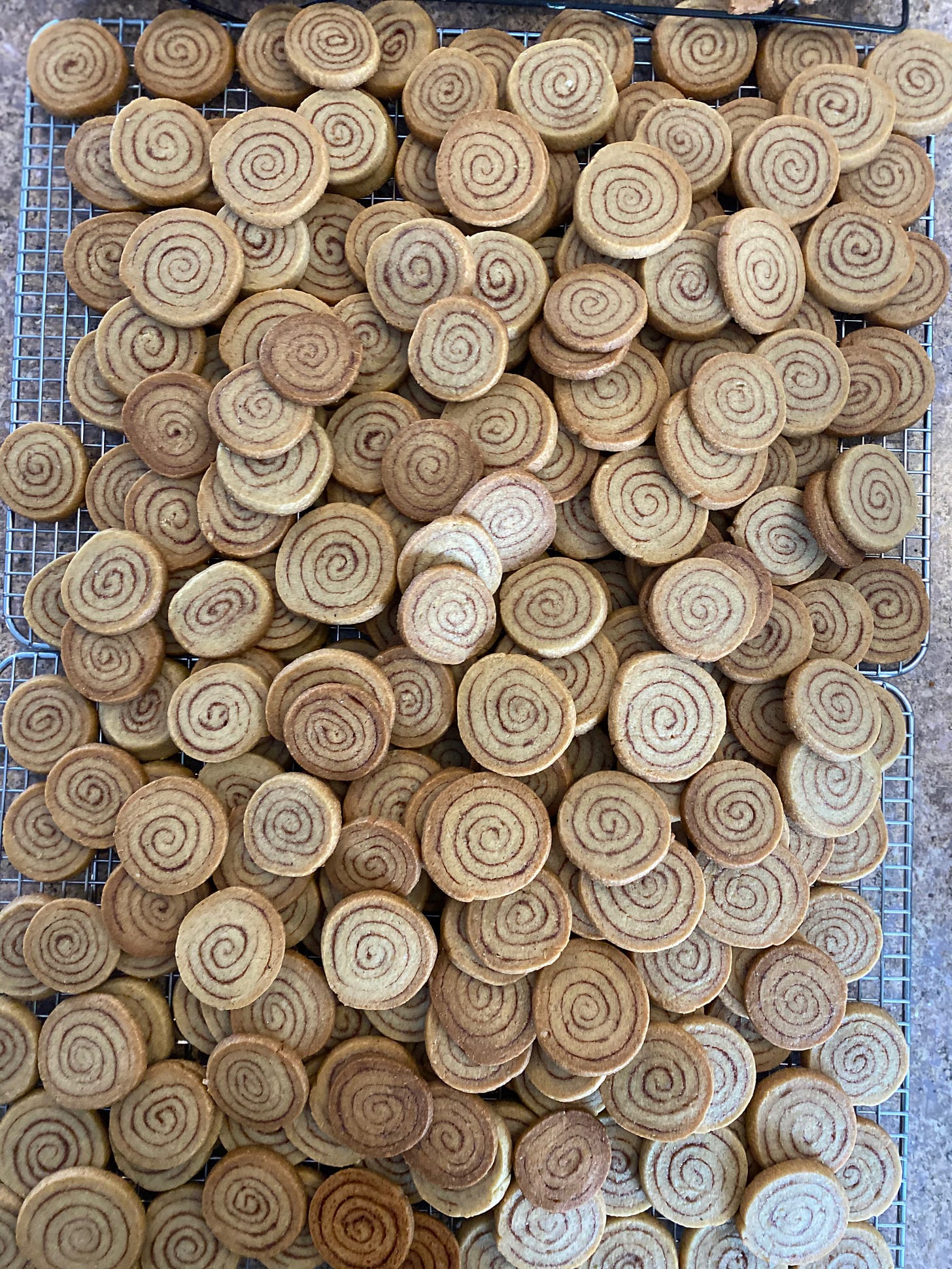A huge pile of small round cookies with a spiral pattern of golden cookie and dark cinnamon filling.