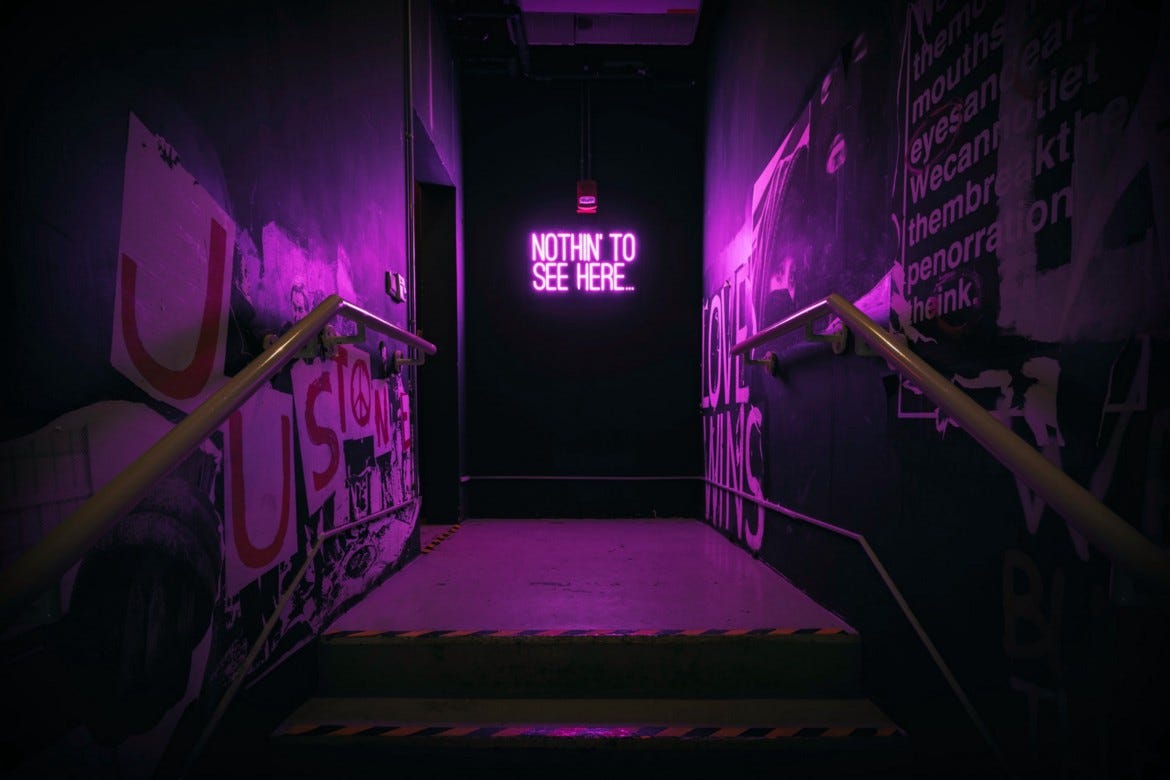 A purple lit hallway with a neon sign at the end saying “Nothin to see here”