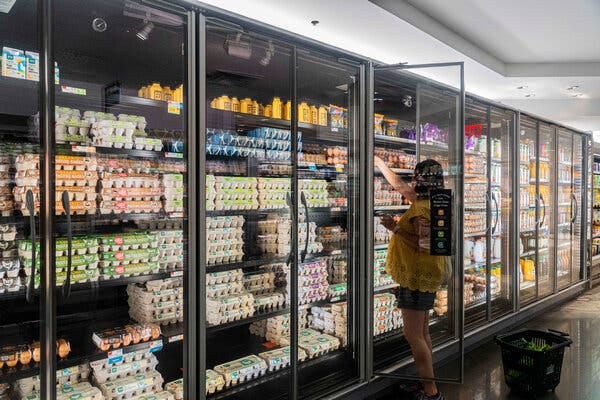 A woman reaching into an open cooler at the grocery store to get eggs.