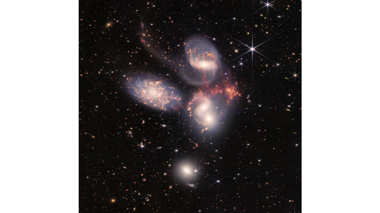 Image of a group of five galaxies that appear close to each other in the sky: two in the middle, one toward the top, one to the upper left, and one toward the bottom. Four of the five appear to be touching. One is somewhat separated. In the image, the galaxies are large relative to the hundreds of much smaller (more distant) galaxies in the background. All five galaxies have bright white cores. Each has a slightly different size, shape, structure, and coloring. Scattered across the image, in front of the galaxies are number of foreground stars with diffraction spikes: bright white points, each with eight bright lines radiating out from the center. For more details, download the Text Description.