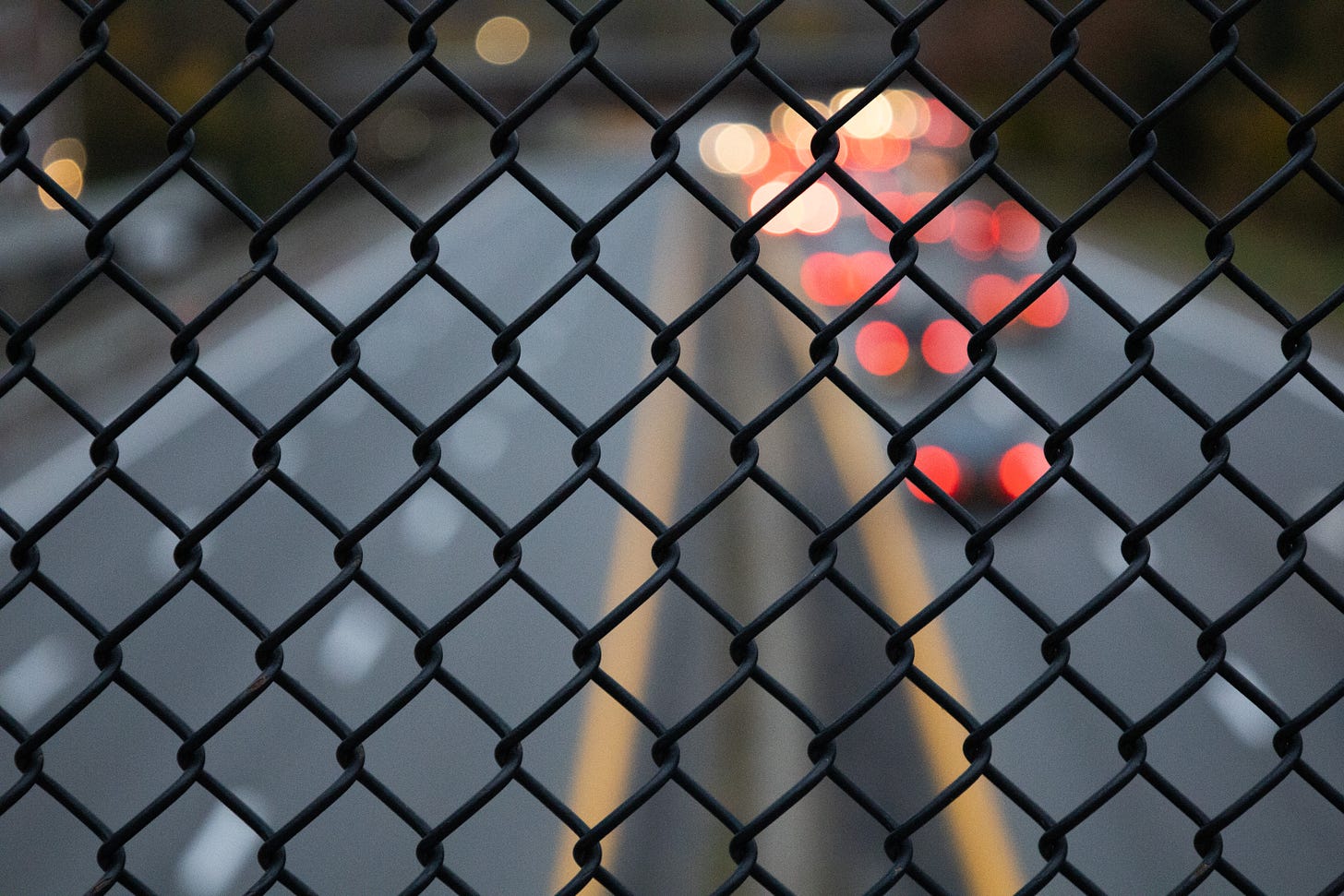 Brake lights out of focus through a chain link fence