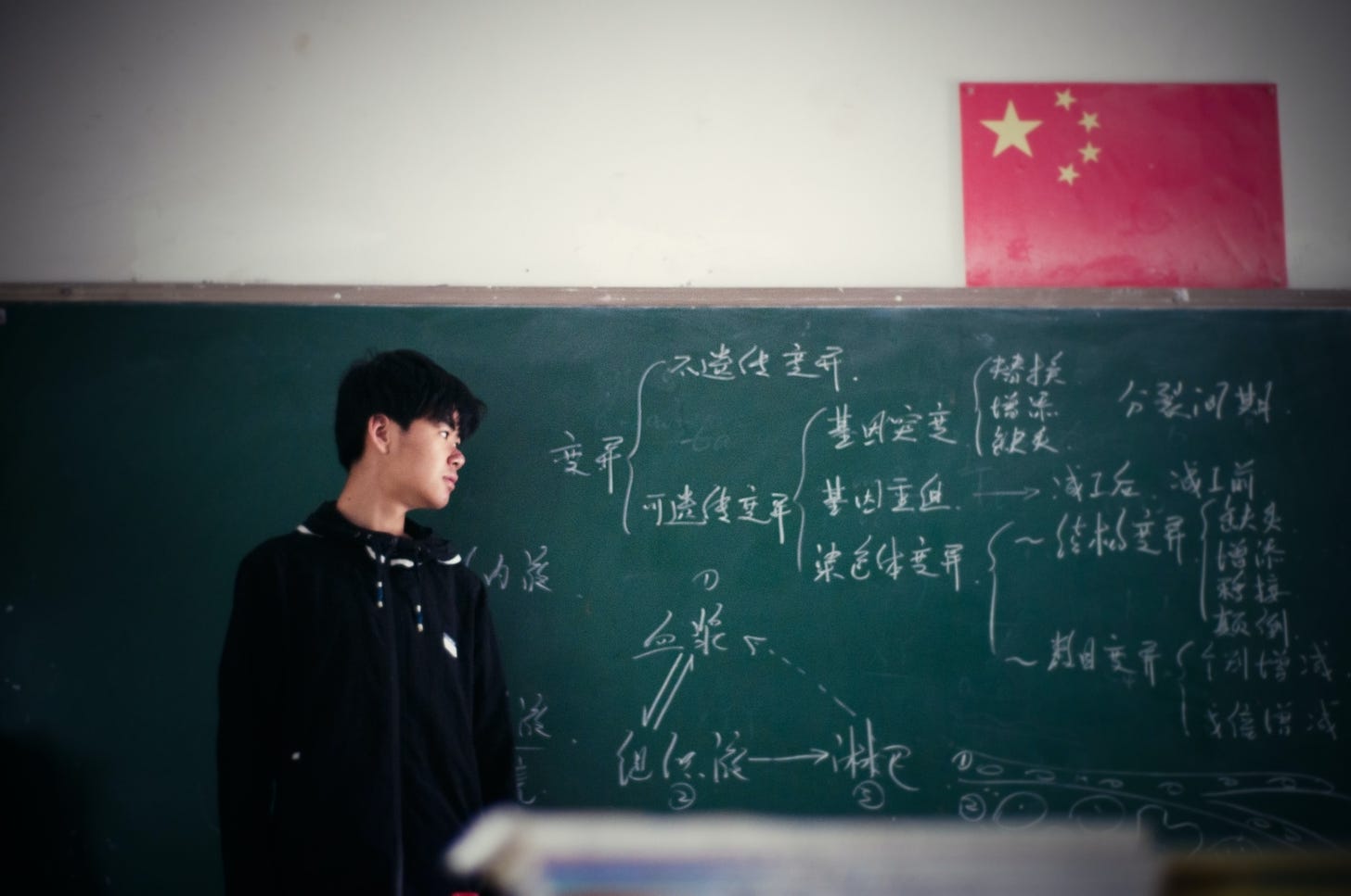 Chinese teacher in front of blackboard with chinese characters.