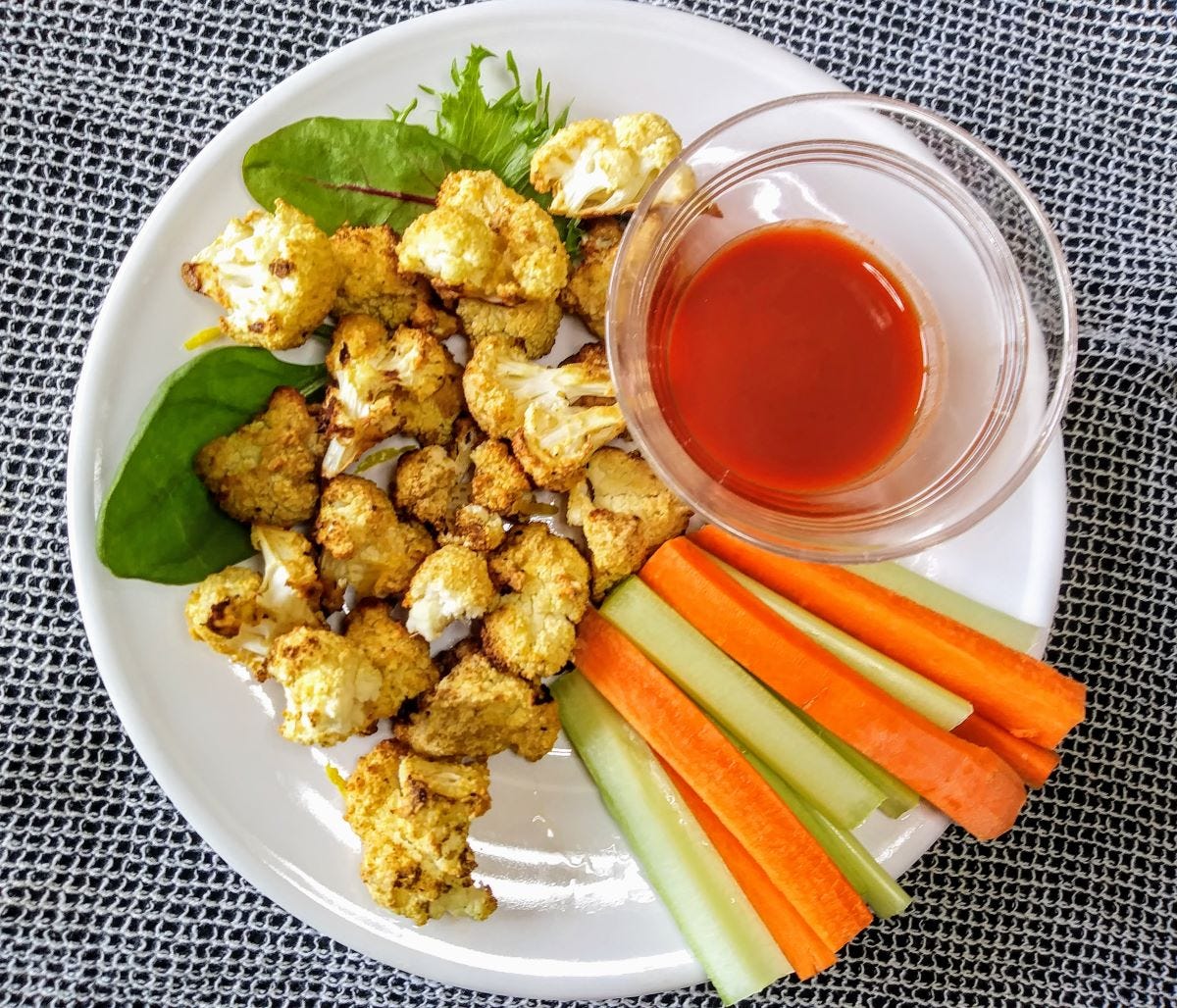 baked crispy cauliflower bites on plate with carrot and celery sticks and hot sauce.