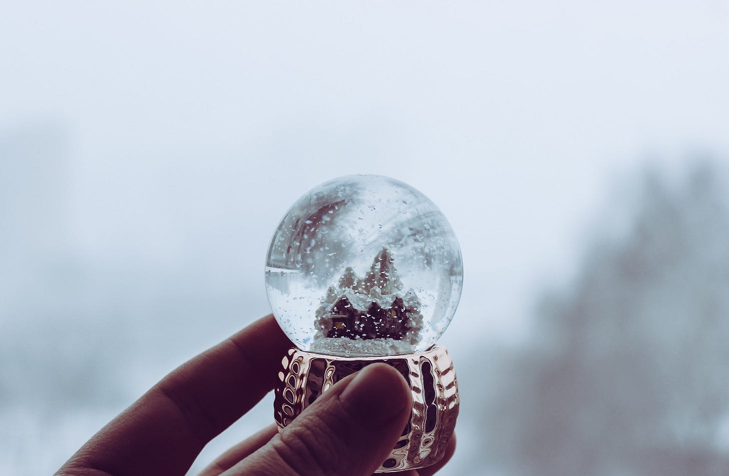 Hand holding small snow globe with a house inside.
