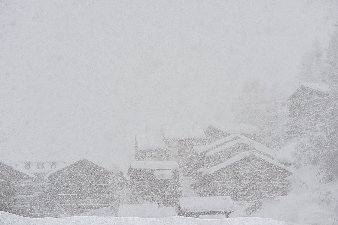 Free Severe scenery of remote rural village houses covered with thick layer of snow during intense snowstorm on cold winter day Stock Photo
