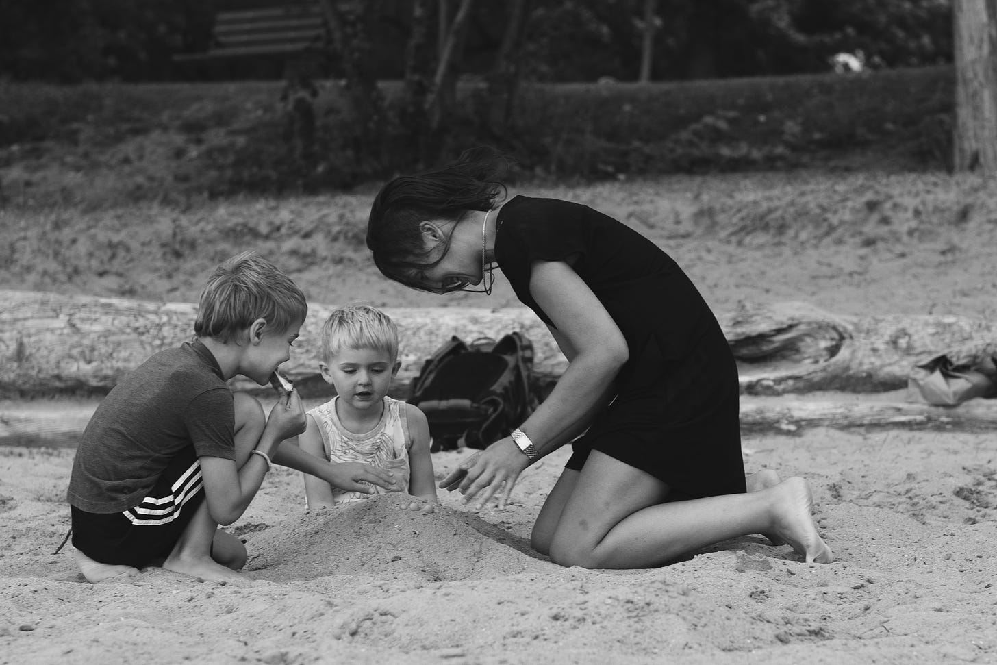 Tarzan plays in the sand with her two young children, both blond-haired boys - they are smiling and having a wonderful time, their hair blowing around in the wind
