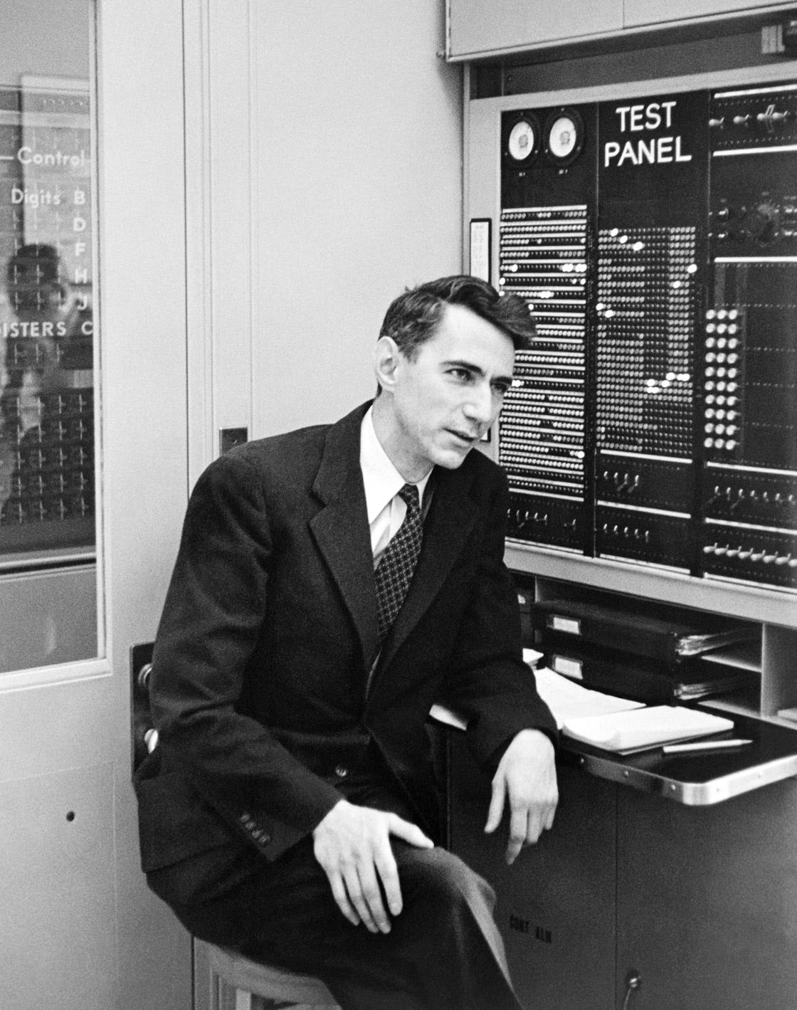 A black-and-white photo of a man sitting in front of an early computer.