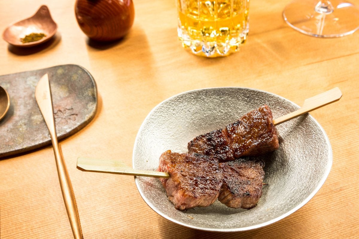 Yakitori-style skewers with cubes of wagyu steak in a shallow ceramic bowl. 