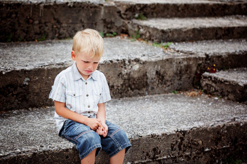 Little Boy crying sitting on stone steps in park. Loneliness, melancholy, stress