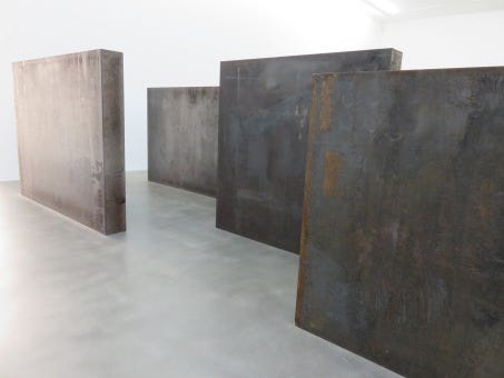Steel Slabs (2015) by Richard Serra, an artwork reflecting the postmodern belief that art is essentially meaningless and so can be jobbed out and made to order, like industrial supplies