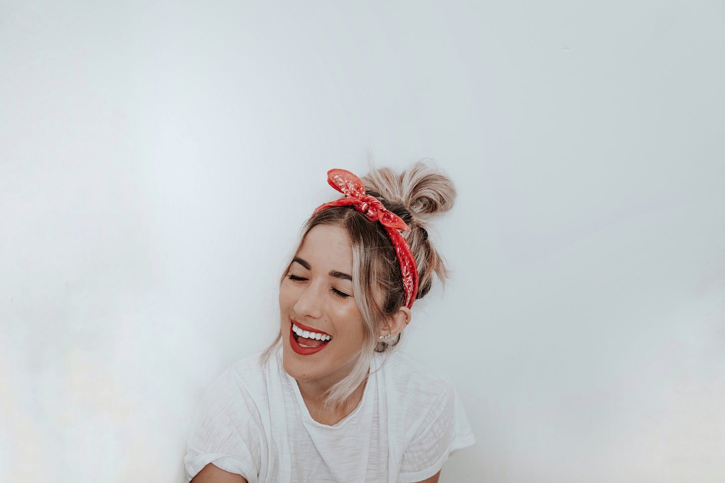 A woman in a red bandana and a white t-shirt smiles against a white background.