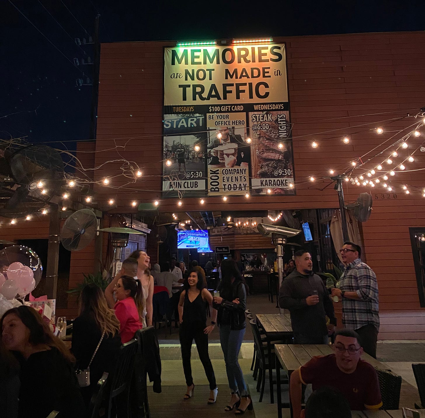 People partying at a bar in Houston, Texas, underneath a sign that says "Memories are not made in traffic."